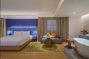 A modern hotel room with a large bed, a sofa, a round table, a bathtub, and a small side table. - Manxin Hotel Yancheng Economic Development Zone (Yancheng)