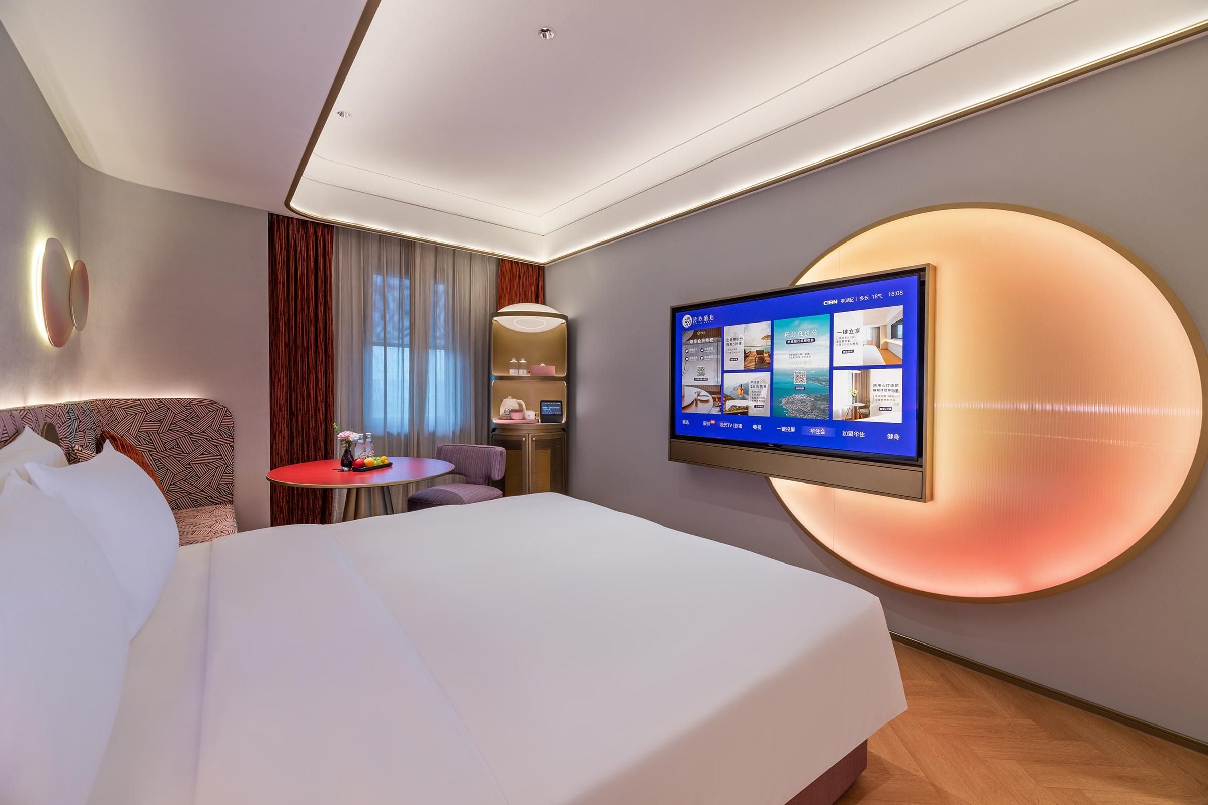 Una habitación de hotel con cama, escritorio, televisor montado en la pared y una lámpara circular grande.