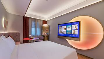 Una habitación de hotel con cama, escritorio, televisor montado en la pared y una lámpara circular grande.