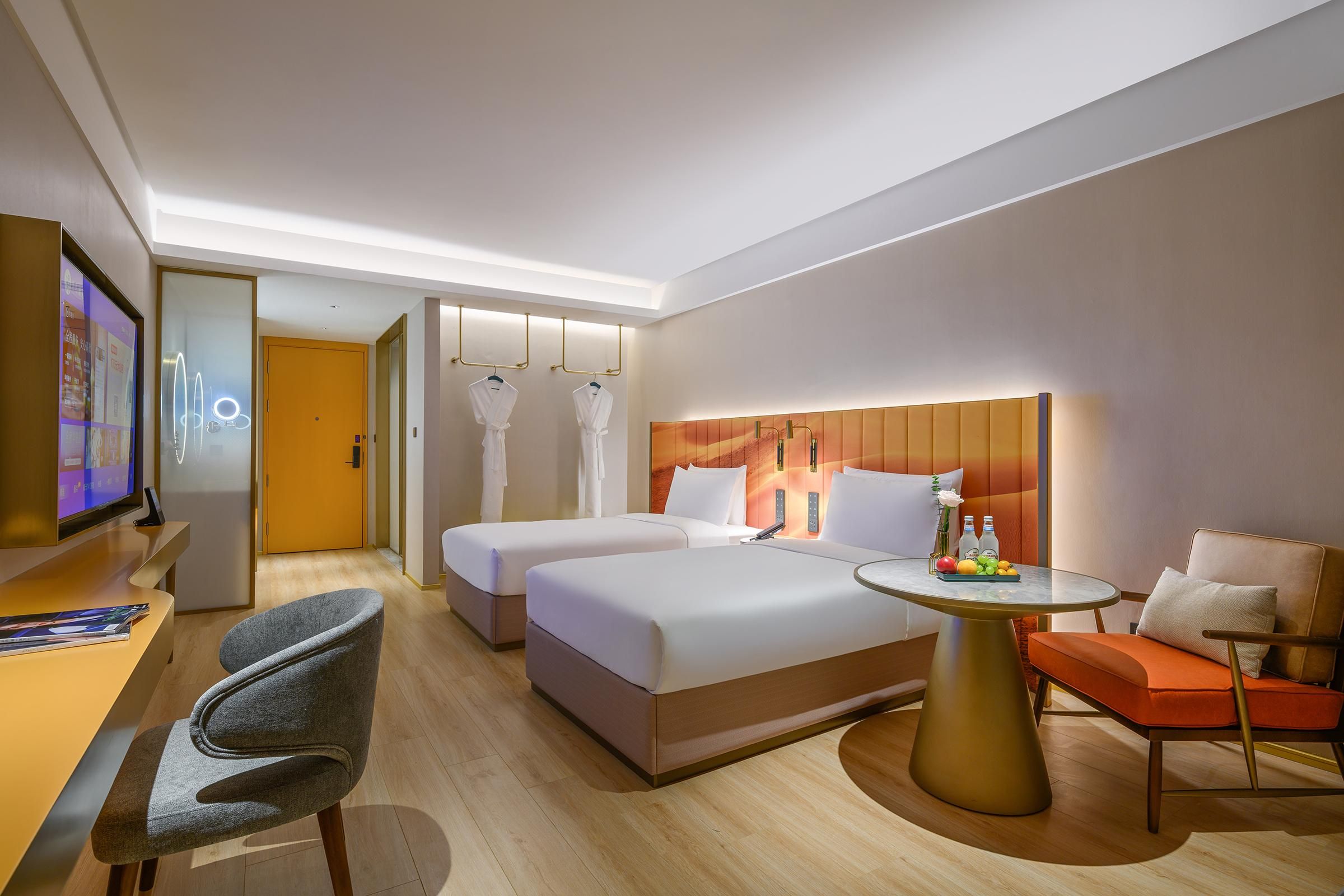 Habitación de hotel con cama, dos mesitas de noche, un escritorio, una silla, una mesita redonda con una bandeja de frutas y un televisor.