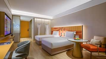 Habitación de hotel con cama, dos mesitas de noche, un escritorio, una silla, una mesita redonda con una bandeja de frutas y un televisor.