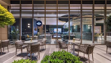Un moderno vestíbulo de hotel con paredes de vidrio, muebles de mimbre y un letrero de Costa Coffee.