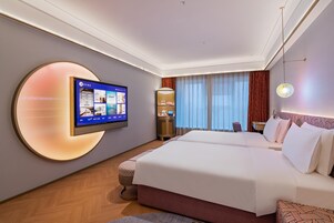 Habitación de hotel con una cama grande, televisión montada en la pared, escritorio con silla y ventana con cortinas.