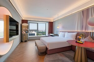 Una habitación de hotel moderna con una cama grande, un escritorio, un televisor y vistas a la ciudad.