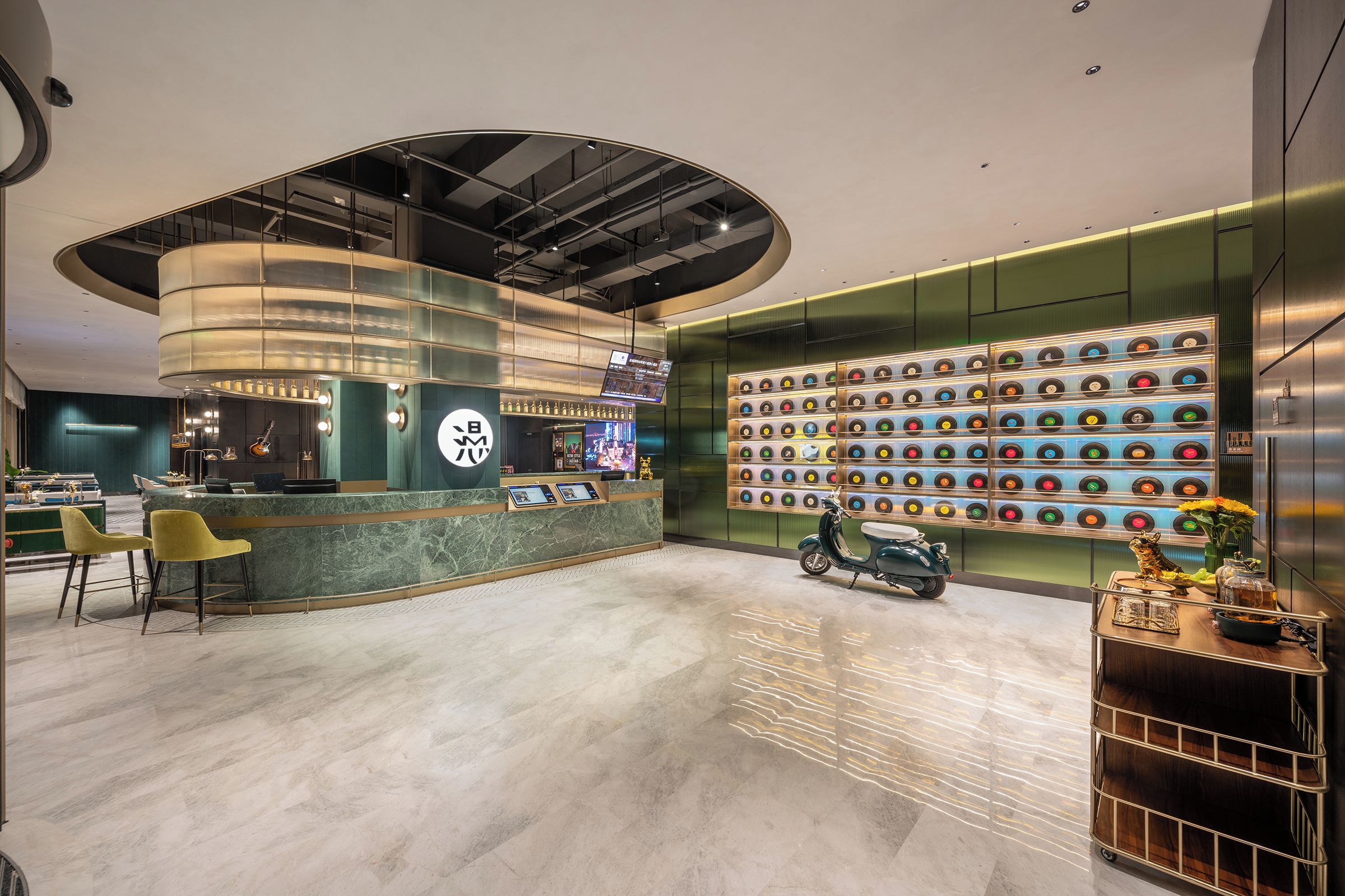 A modern reception area with a curved counter, a wall of vinyl records, and a scooter.