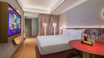 Una habitación de hotel con una cama grande, un televisor montado en la pared, una mesa redonda con fruta y un espejo con marco decorativo.