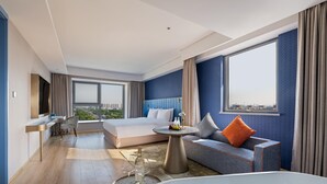 Una habitación de hotel moderna con una cama grande, un sofá, una mesa redonda de centro y una bañera, con vistas a la ciudad.