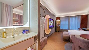 Quarto de hotel com um espelho grande, televisão, cama, sofá e uma mesinha.