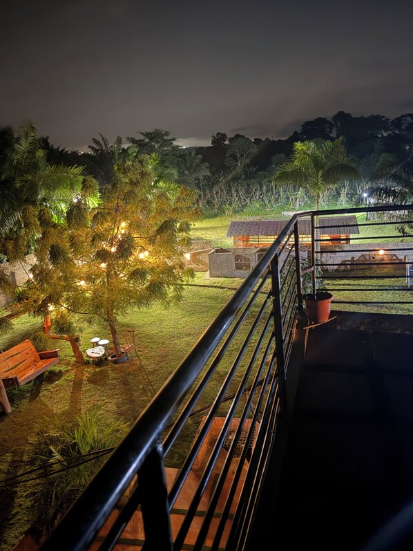 A nighttime view of a garden with a wooden bench, a small table, and a building with a corrugated roof.