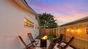 A backyard patio with a fire pit, outdoor seating, and a wooden fence.