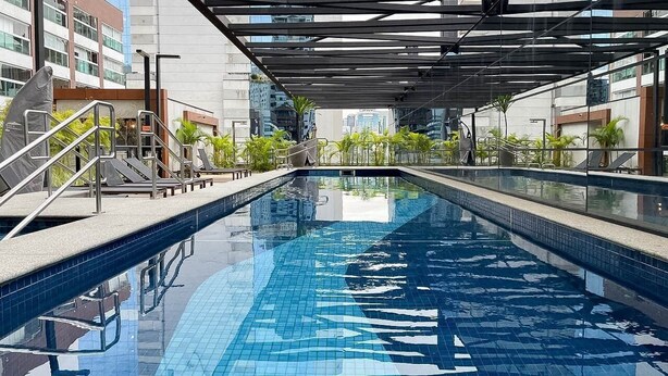 A modern indoor swimming pool with clear blue water, surrounded by glass walls and metal railings. - Nun Vila Nova 2503 - Vila Nova Conceição (São Paulo)