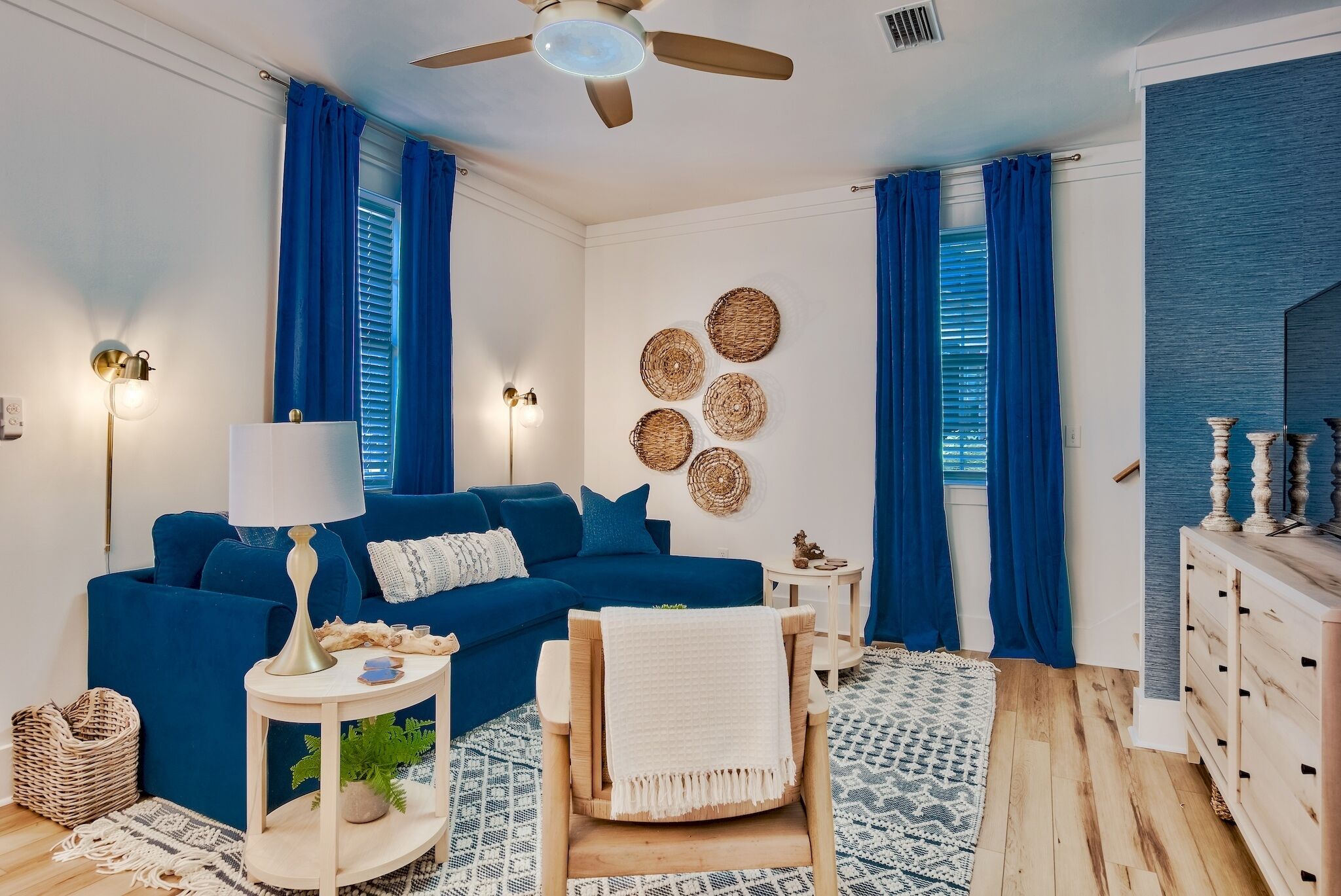 A modern living room with a blue sofa, a wooden chair, a small side table, and a ceiling fan.