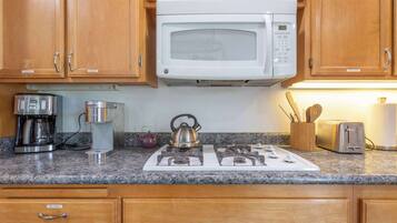 A kitchen with wooden cabinets, a white microwave, a gas stove, a coffee maker, a kettle, and a toaster.