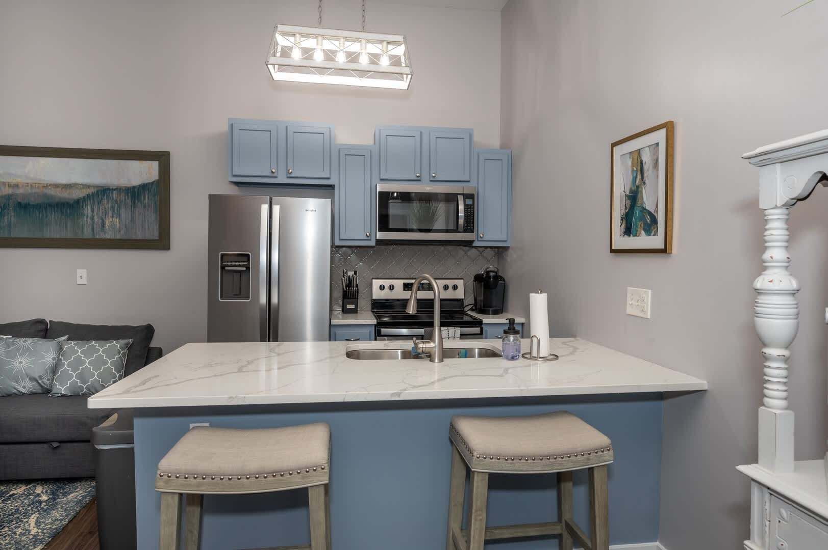 Una cucina moderna con mobili blu, elettrodomestici in acciaio inossidabile, un piano di lavoro in marmo e uno sgabello da bar.