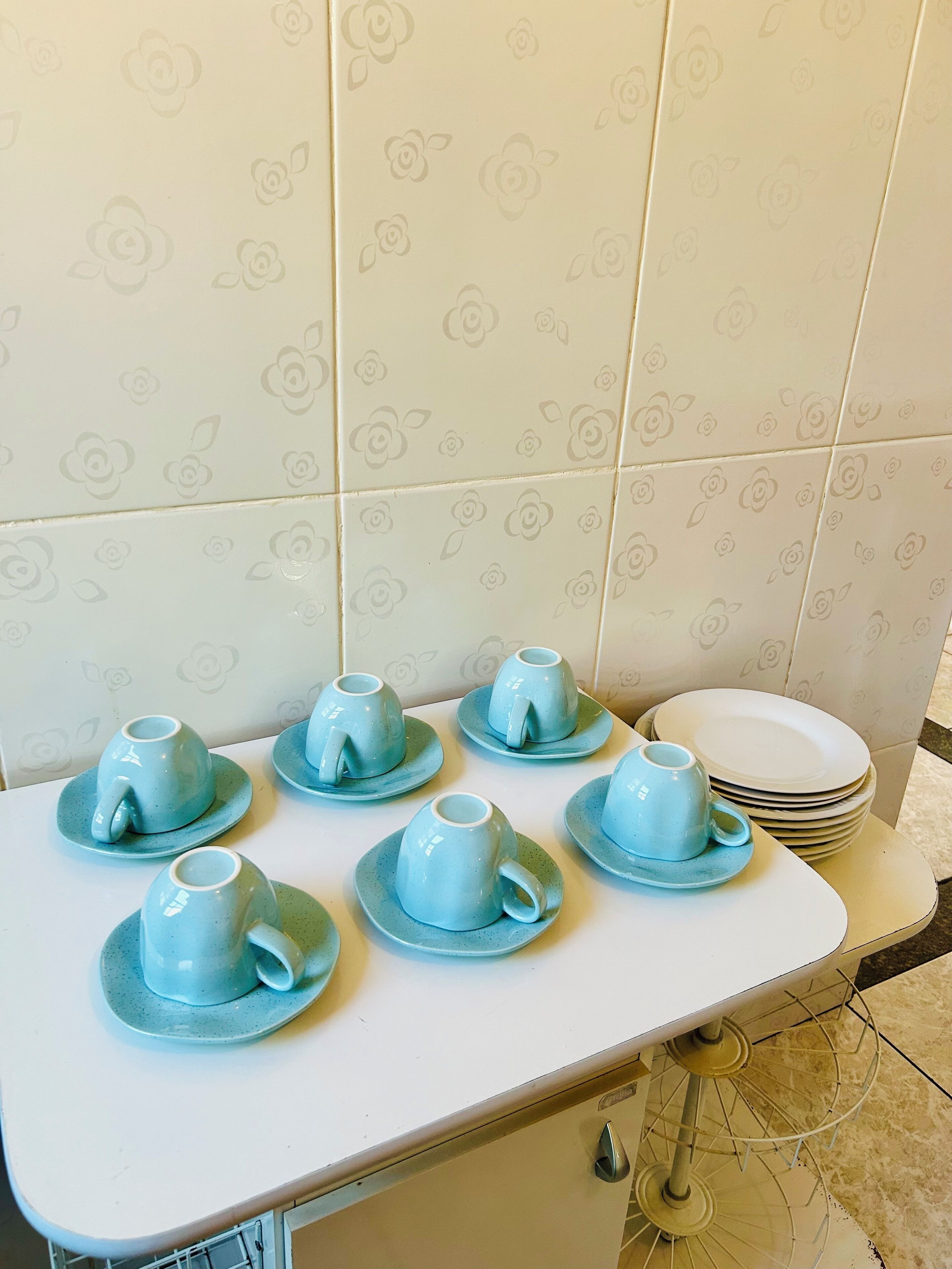 Una cocina con cubierta blanca, seis tazas azules con platillos y una pila de platos blancos.