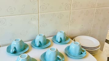 Una cocina con cubierta blanca, seis tazas azules con platillos y una pila de platos blancos.