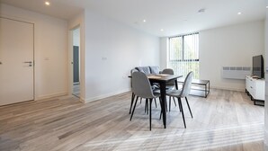 A modern, well-lit dining area with a wooden table and chairs, a small side table, and a built-in TV. - GuestReady - Tranquil Vauxhall Stay (Liverpool)