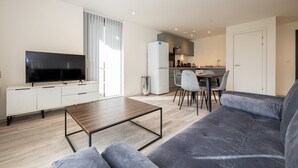 A modern living room with a flat-screen TV, a sofa, a coffee table, and a dining area with chairs and a kitchen in the background. - GuestReady - Tranquil Vauxhall Stay (Liverpool)