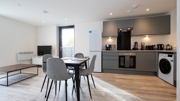 A modern kitchen with a built-in oven, microwave, and washing machine. There is a dining area with a table and chairs. - GuestReady - Tranquil Vauxhall Stay (Liverpool)