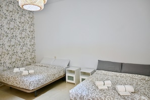 Una habitación de hotel con dos camas, cada una con una colcha y almohadas estampadas, y una mesita de noche blanca pequeña entre ellas.