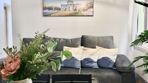 Una sala de estar moderna con un sofá gris, un jarrón blanco con flores y una lámpara colgante.