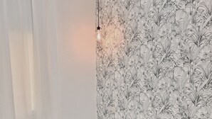 Un dormitorio con papel tapiz estampado, una cama con colcha estampada, una mesita de noche y una lámpara colgante.