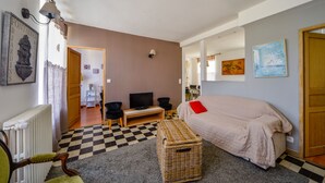 Ein gemütliches Zimmer mit Schachbrettmuster-Boden, einem Bett mit rotem Kissen, einem Fernseher und einem Korbwäschekorb.
