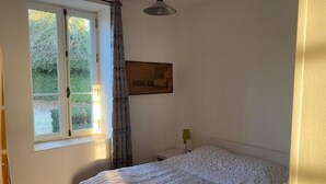 Ein Schlafzimmer mit Bett, einem Fenster mit Vorhängen, einer Nachttischlampe und einer Heizung.