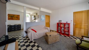 Ein Zimmer mit Schachbrettmuster-Boden, einem abgedeckten Sofa, einem roten Bücherregal, einem Korbwäscher und einem grünen Sessel.