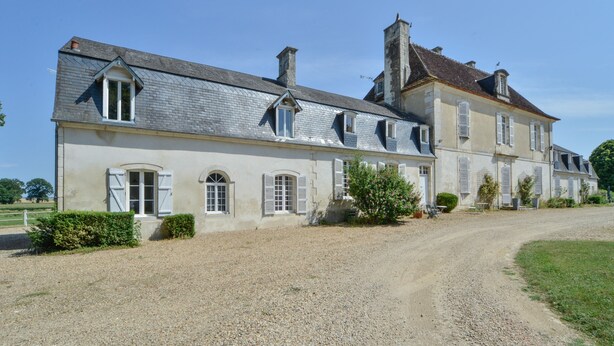 A large, historic building with a gravel driveway and a well-maintained lawn.