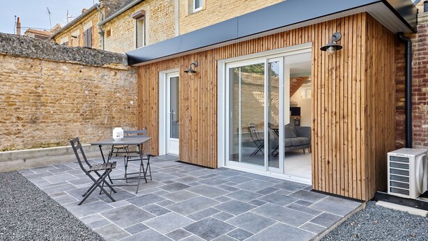 A modern outdoor patio area with a stone floor, wooden panel walls, and a glass sliding door leading to an interior space.