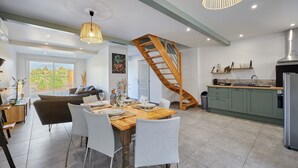 A modern kitchen with a wooden staircase, a dining area with white chairs, and a view of the outdoors.