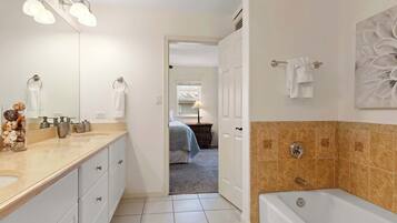 A bathroom with a double sink, a bathtub, and a large mirror.