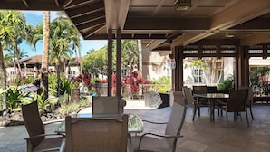An outdoor patio area with chairs and tables, surrounded by tropical plants and a pool. - Honu Harmony Pools, Golf Privileges, & More (Waikoloa)