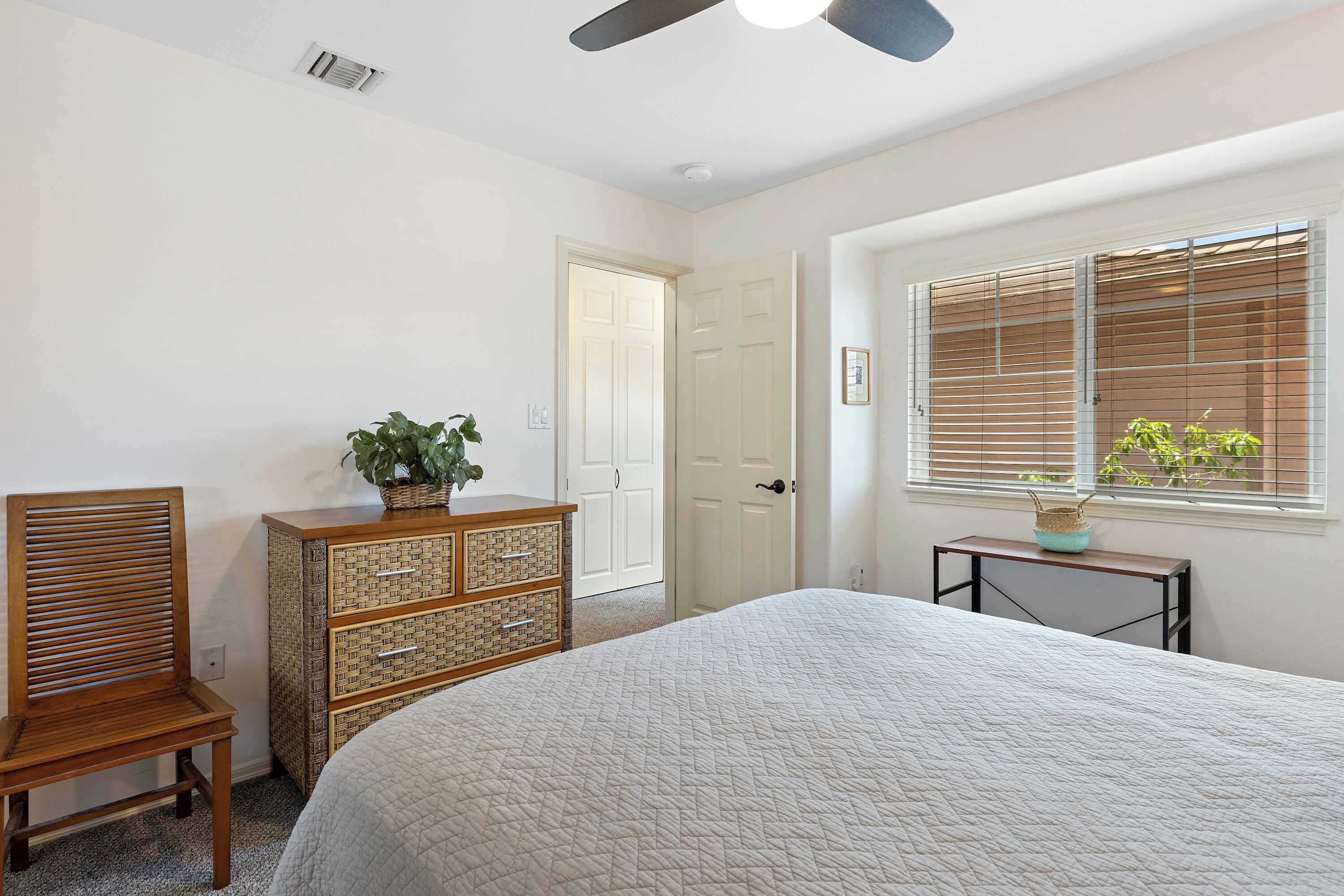 A bedroom with a bed, a wooden chair, a dresser, a window with blinds, and a ceiling fan.