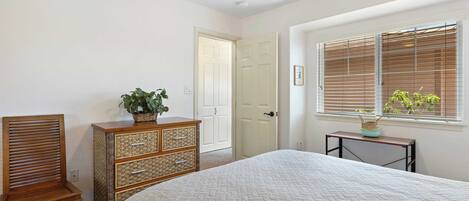 A bedroom with a bed, a wooden chair, a dresser, a window with blinds, and a ceiling fan.