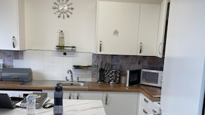 Et moderne køkken med hvide skabe, en marmor bordplade, indbygget mikrobølgeovn og et lille spiseområde med bord og stole.
