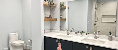A modern bathroom with two sinks, a toilet, and a shower.