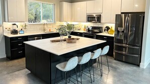 A modern kitchen with white cabinets, a central island with bar stools, a stainless steel refrigerator, and a microwave. - Stunning 'Ranch Modern' + Stars! + Firepit! (Driftwood)