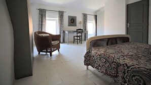 A bedroom with a bed, a chair, a desk, and a door. - Logement Touristique Villa Eugénie (Lezignan-Corbieres)