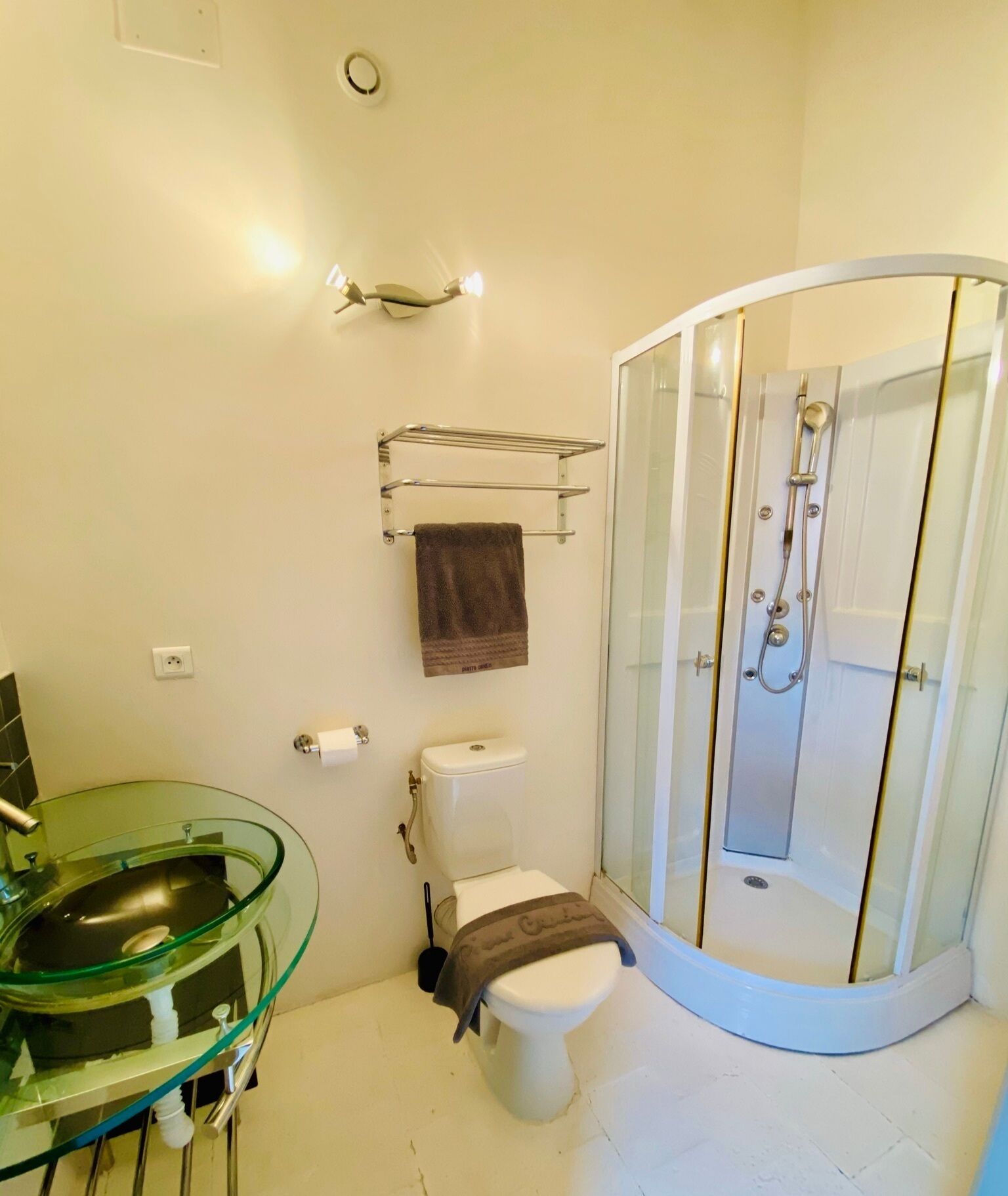 A bathroom with a glass sink, a toilet, a shower enclosure, and a towel rack.