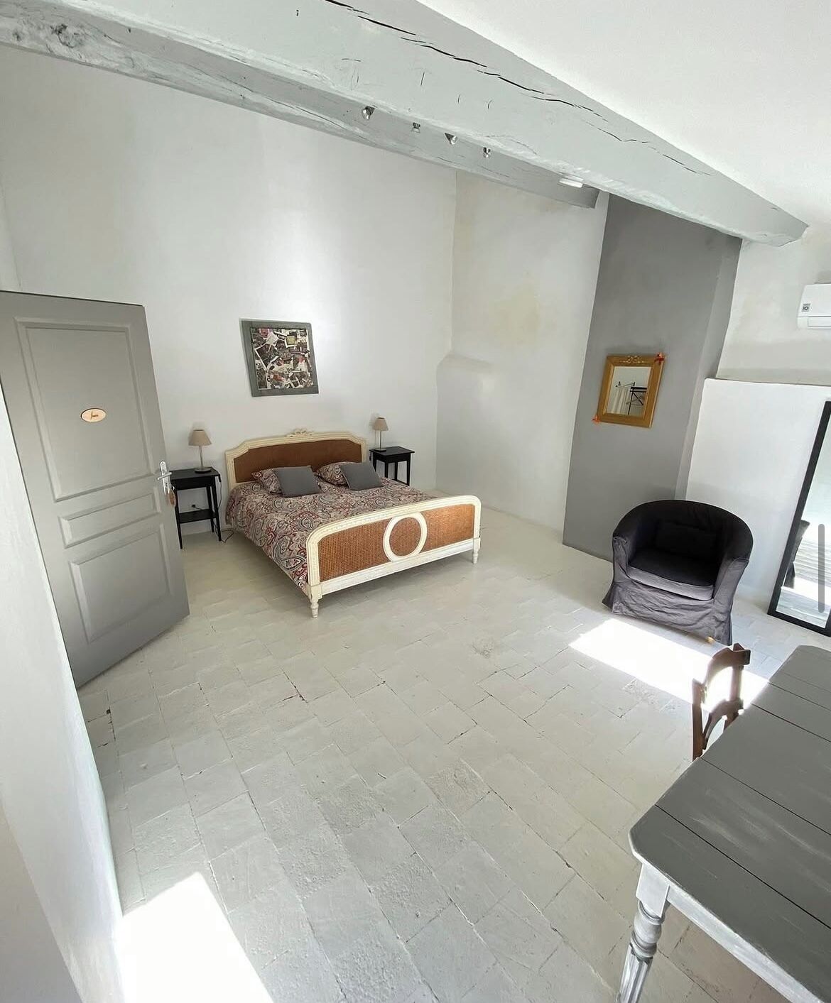 Un dormitorio con cama, mesitas de noche, una silla, un escritorio y una puerta.