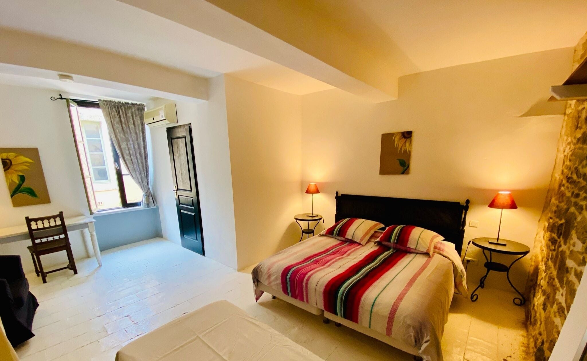 Un dormitorio con cama, dos lámparas de noche, una ventana con cortinas, una silla y un cuadro en la pared.
