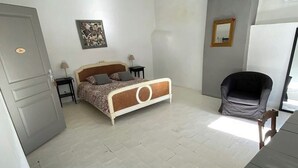A bedroom with a bed, bedside tables, a chair, a mirror, and a door. - Logement Touristique Villa Eugénie (Lezignan-Corbieres)