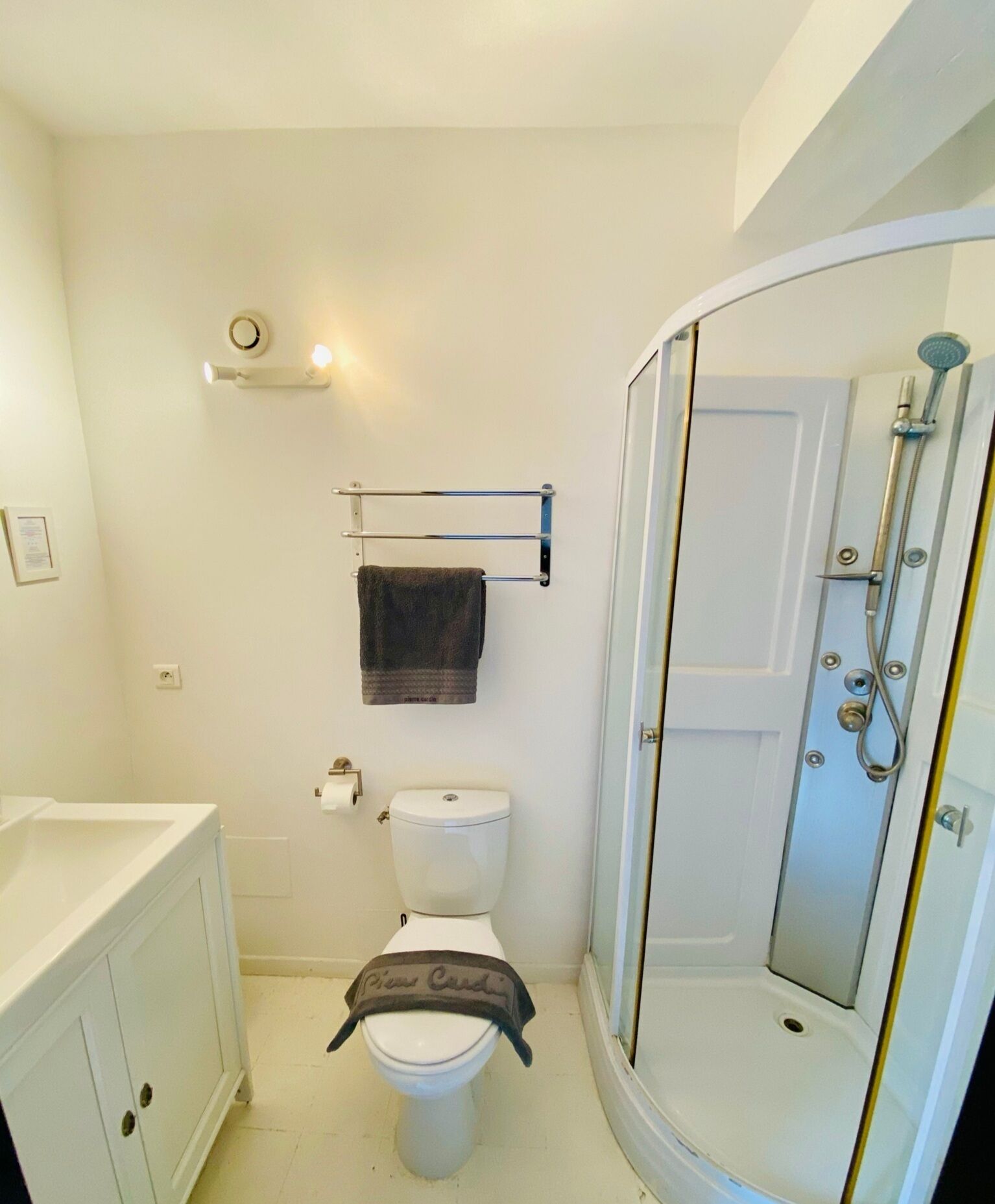Une petite salle de bain comprenant des toilettes, un porte-serviettes, un espace douche et un lavabo blanc.