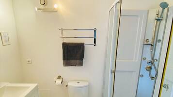 Une petite salle de bain comprenant des toilettes, un porte-serviettes, un espace douche et un lavabo blanc.