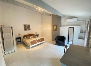 A bedroom with a bed, bedside tables, a chair, a desk, and an air conditioning unit.