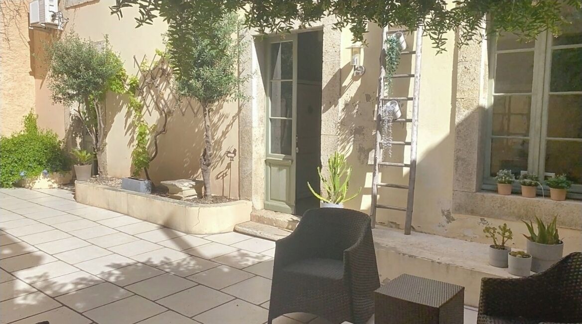 Un espace extérieur aménagé en terrasse, doté d’un sol carrelé, de meubles en osier et de plantes en pot.