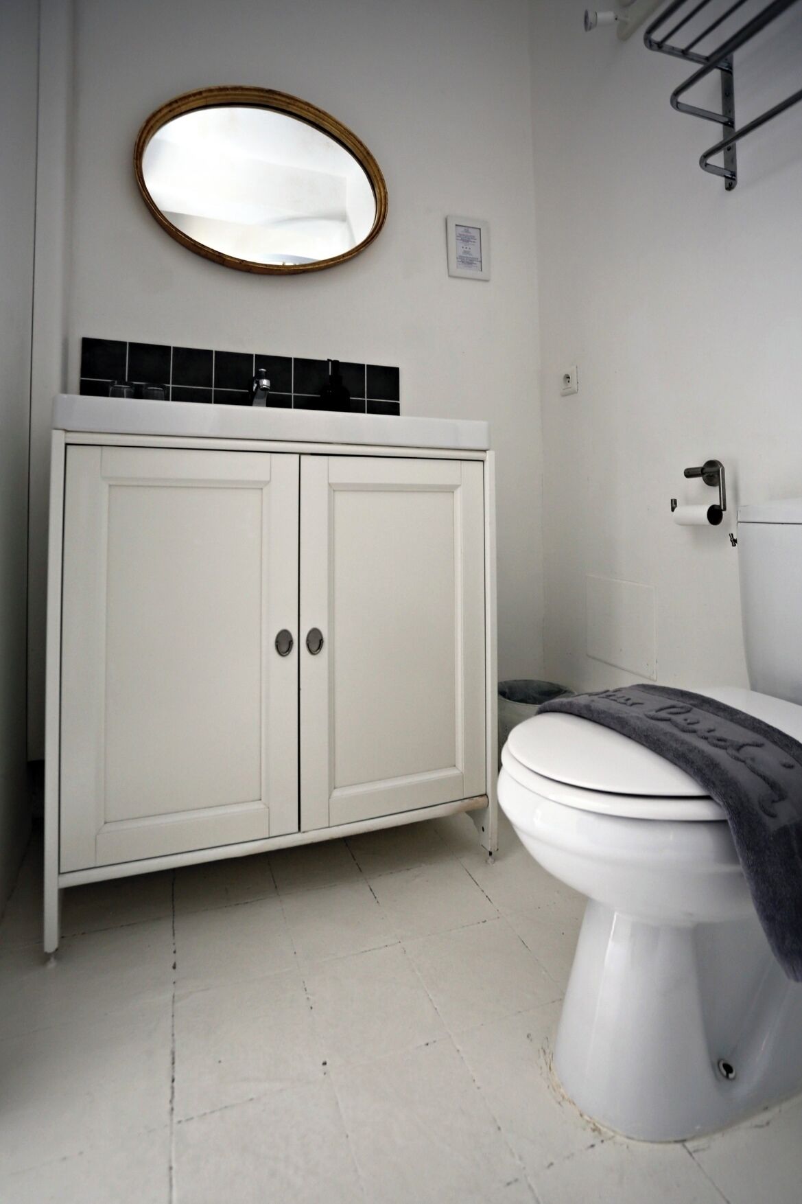 A bathroom with a white cabinet, a round mirror, a toilet, and a towel rack.