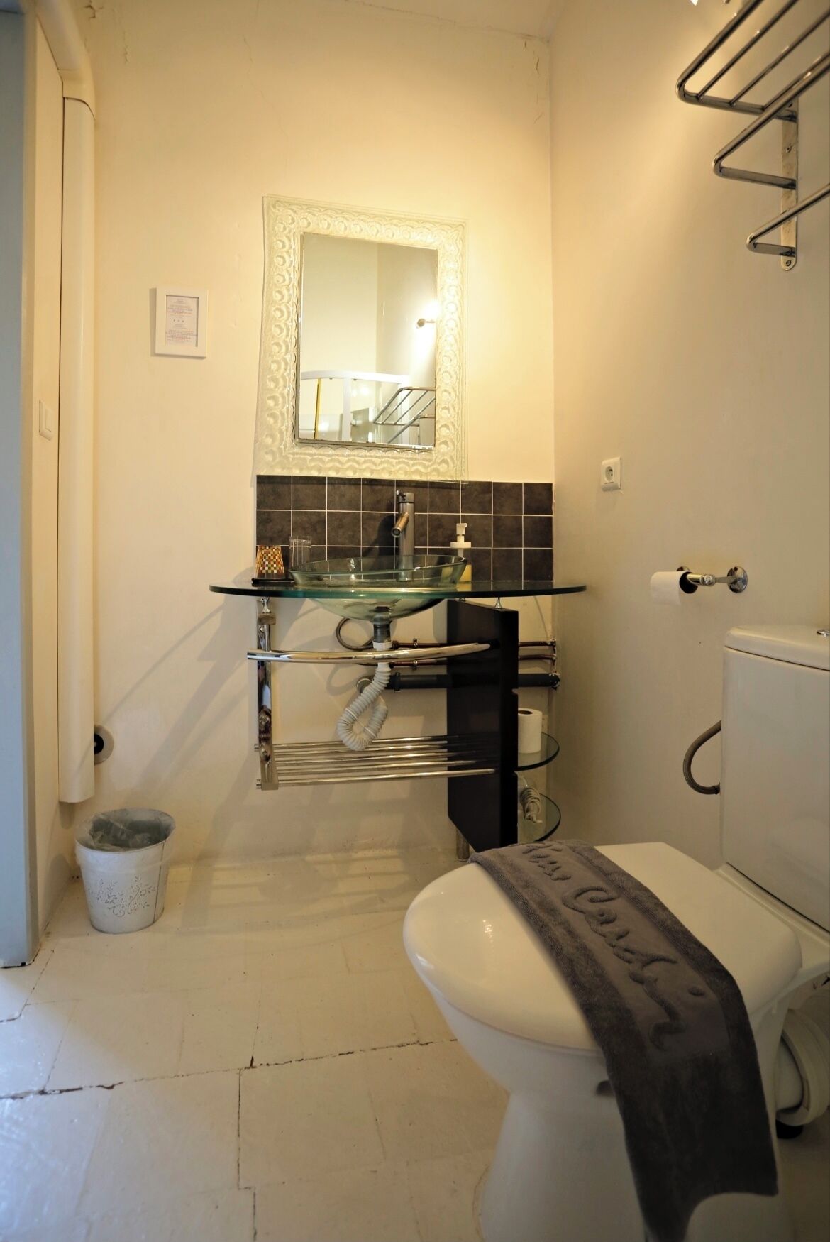 Une salle de bain avec un lavabo en verre, des toilettes, une poubelle et un porte-serviettes.
